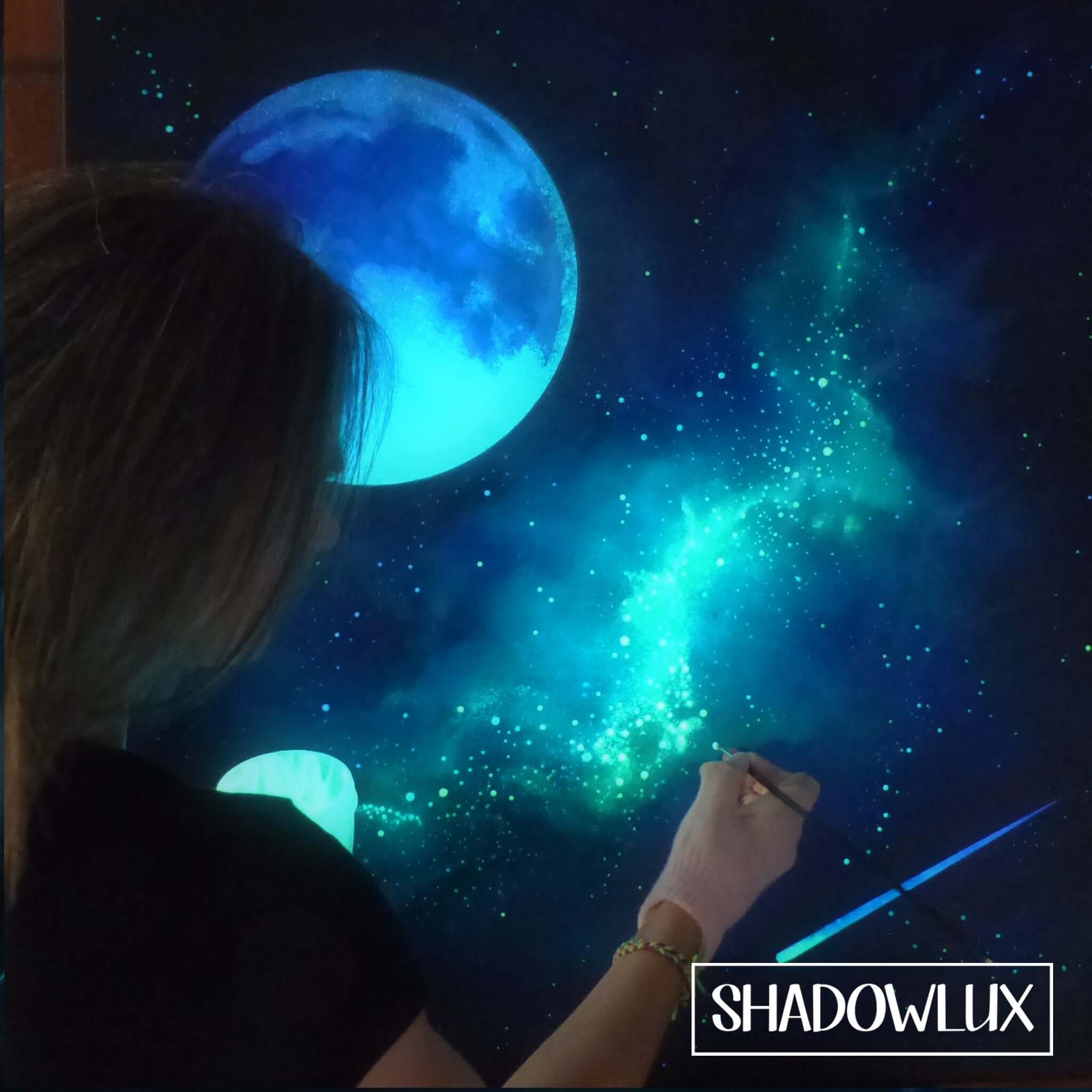 Person painting a glow in the dark artwork of a celestial scene with a blue moon and shooting star