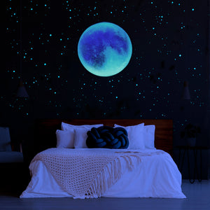 Large glow in the dark Ombre coloured moon with glow in the dark stars on a dark bedroom wall. The glow stars are uv charged and are blue and green, unique bedroom decor for night time. 